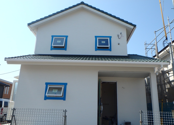 緑の瓦と青の窓モールがアクセントの家